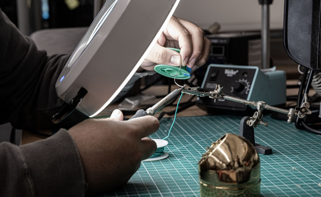 Hand-soldering a V1 tracker PCB under a magnifier lamp